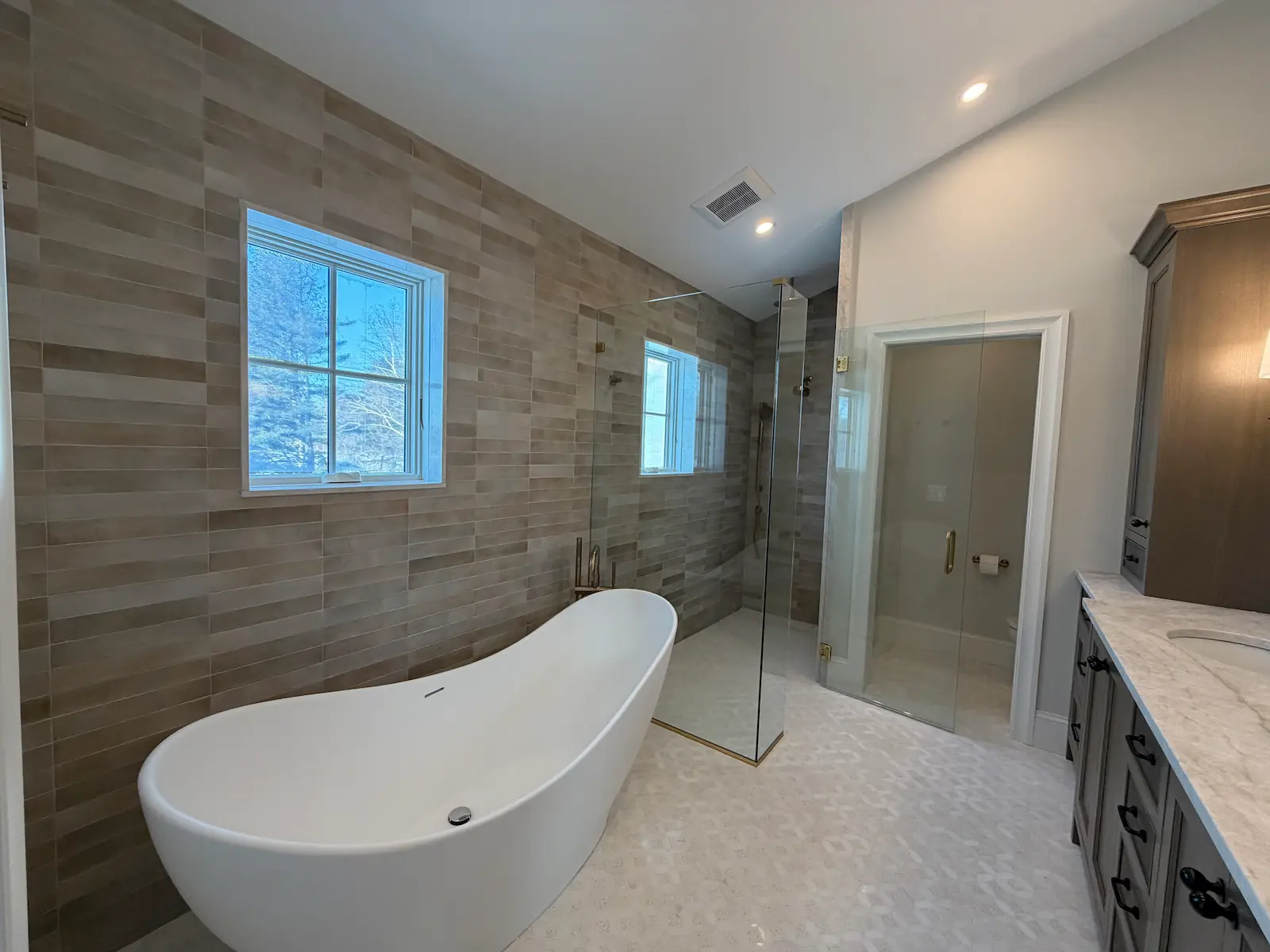 Completed bathroom tile installation in Brookline, MA — freestanding tub, porcelain plank accent wall, glass walk-in shower, and mosaic floor tile by Davie Mac Tile