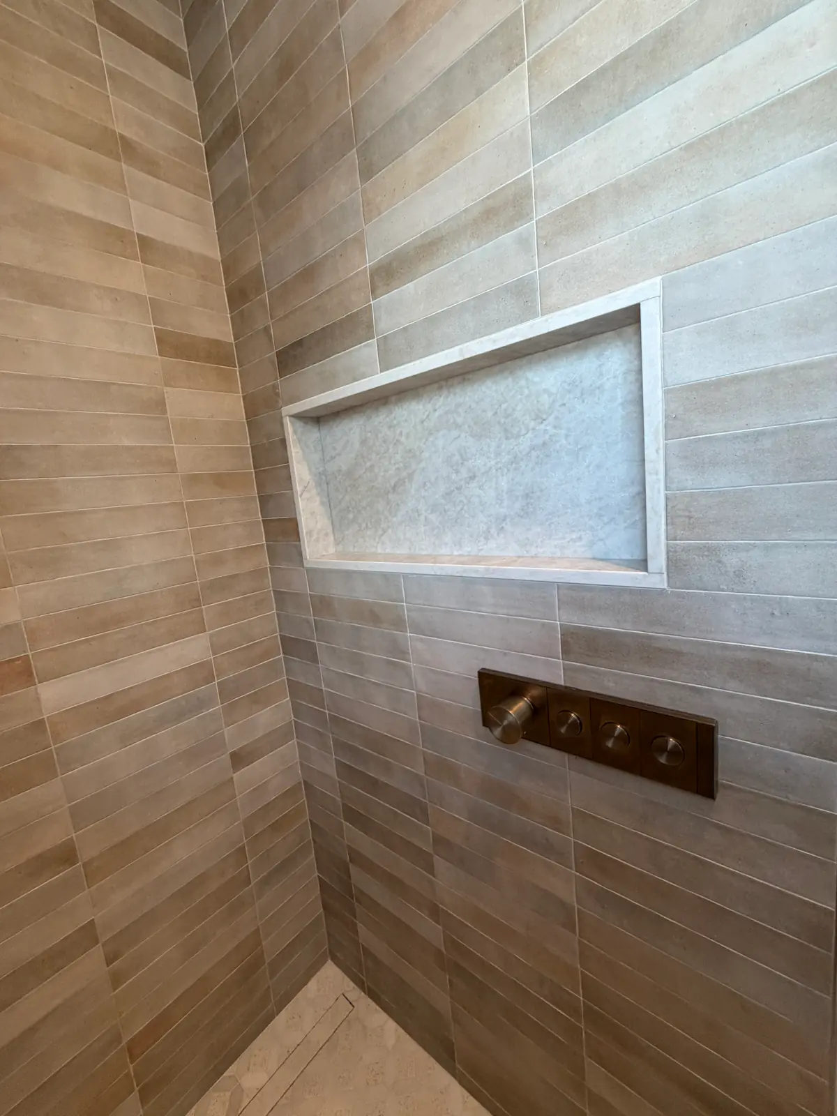 Shower niche detail with natural stone accent tile and brass valve controls — Brookline, MA bathroom tile installation by Davie Mac Tile