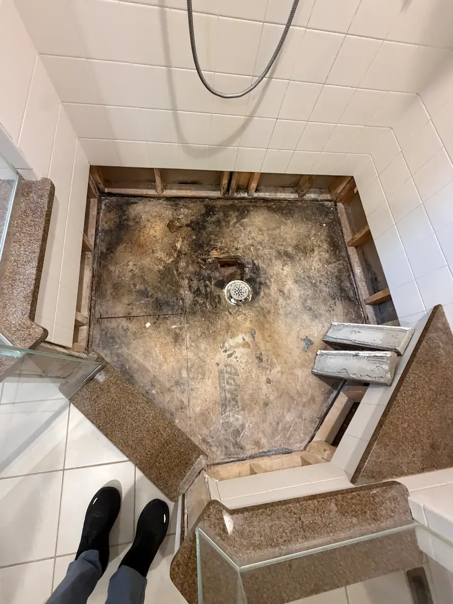 Failed shower pan in Scituate, MA, mud bed on tar paper with dark water staining around the drain