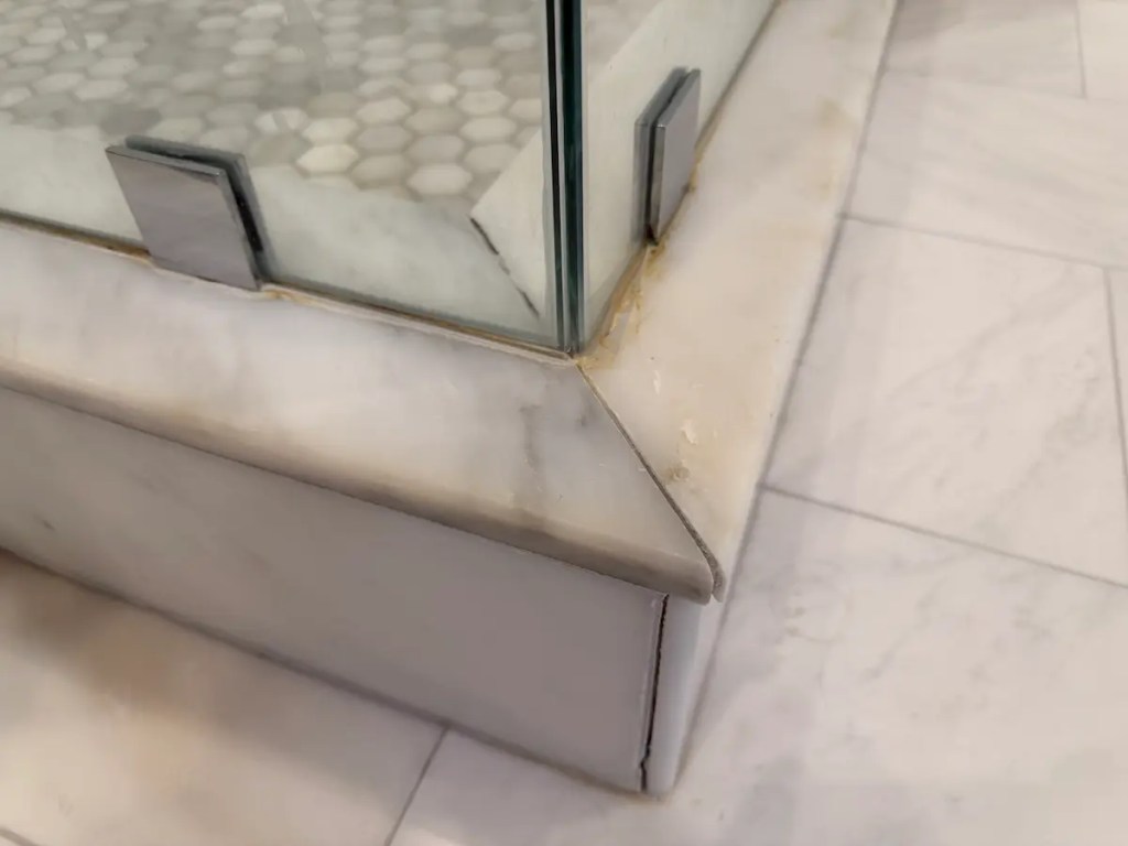 Marble shower curb with cracked grout and poor caulking from unqualified tile installation in Massachusetts