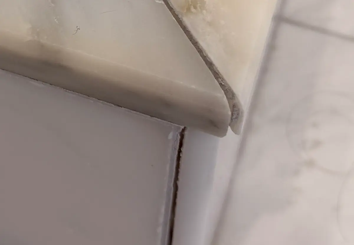 Close-up of damaged marble shower curb corner showing tile separation and water infiltration from improper installation