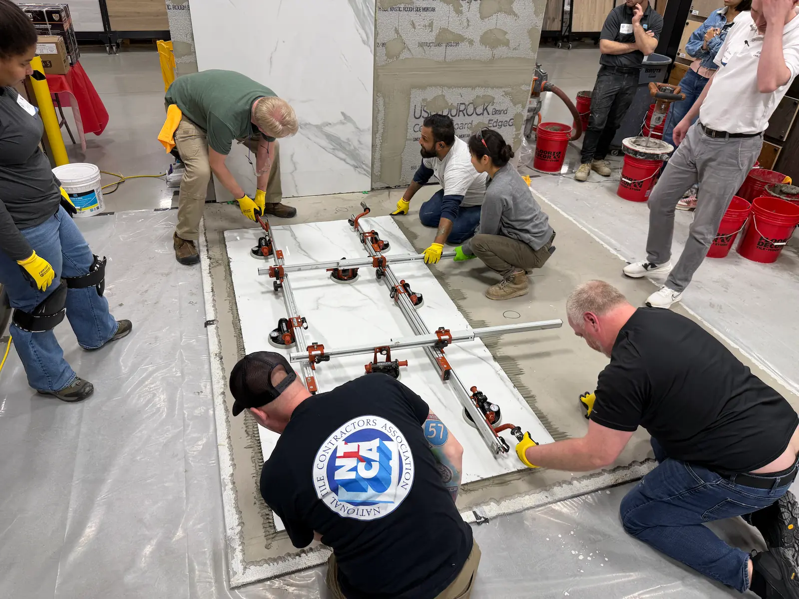 Two Davie Mac Tile installers practicing gauged porcelain slab installation on floor during NTCA training, March 2026