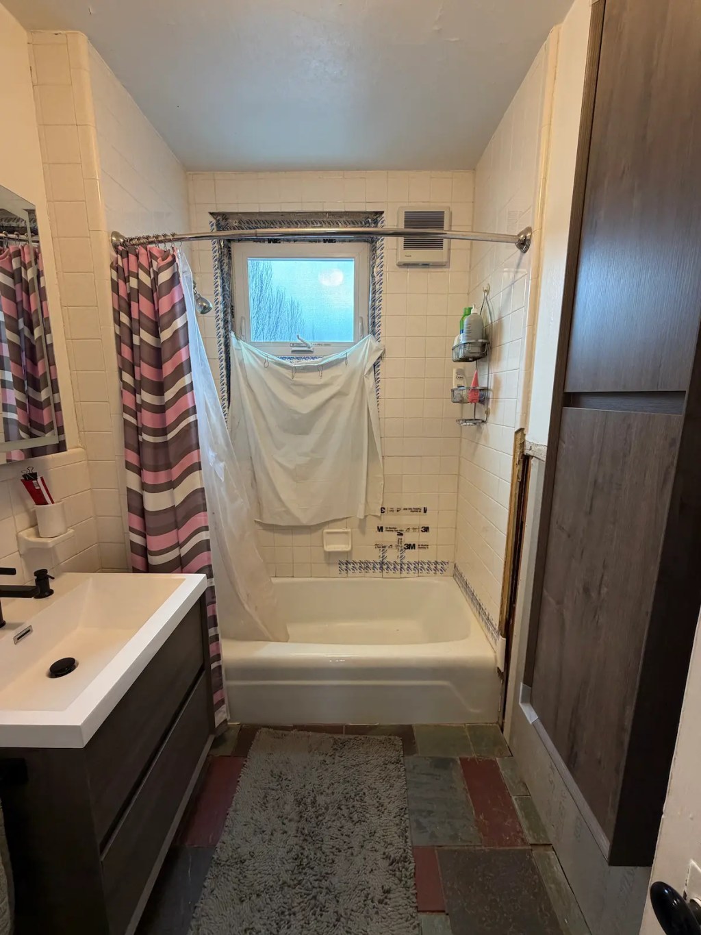 Outdated Somerville bathroom before tub-to-shower conversion, with failing wall tile held up by tape.