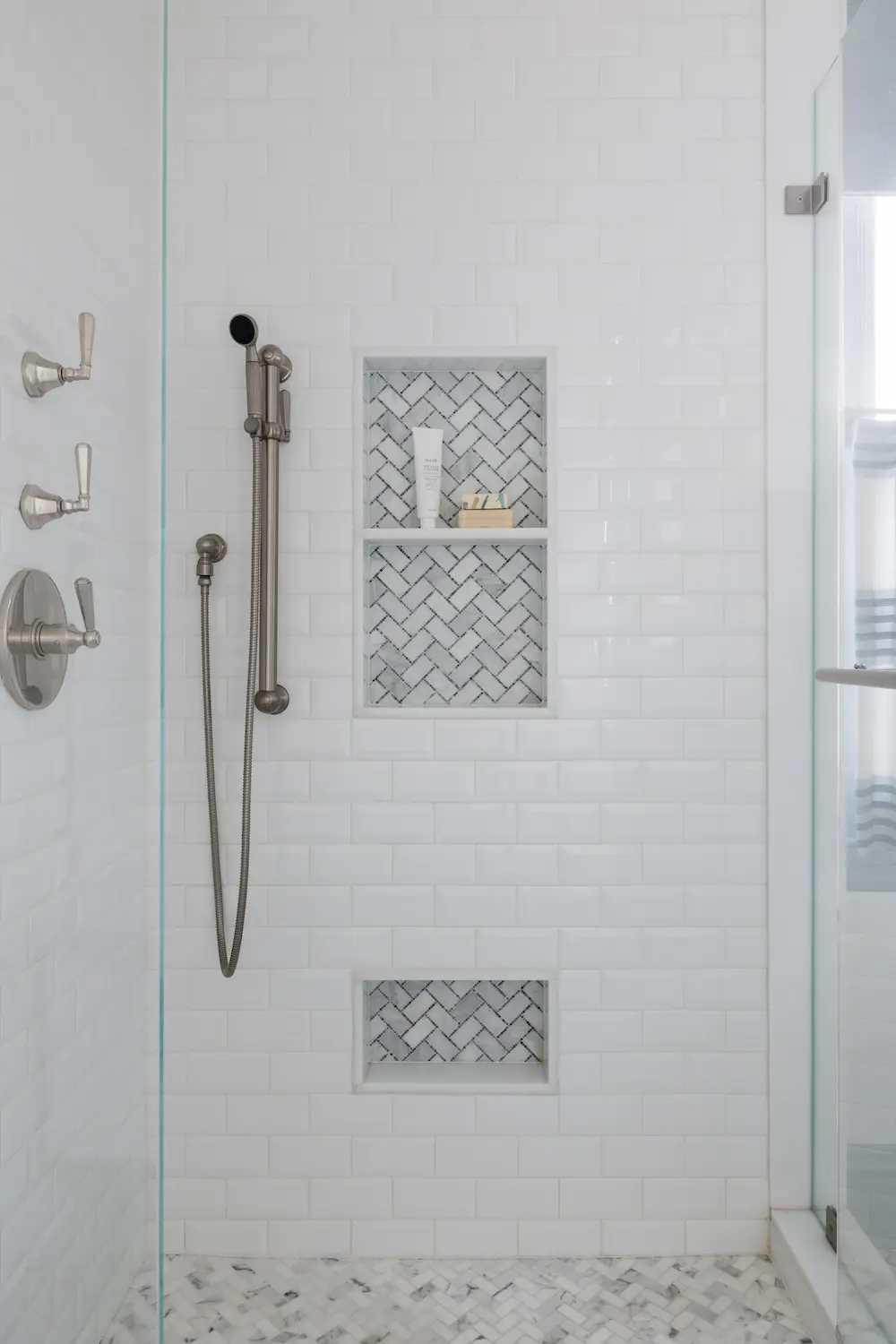 Elegant white subway tile shower with marble herringbone niche, professionally installed by Davie Mac Tile.